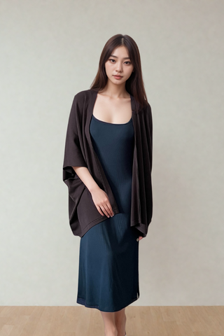 A woman stands indoors against a plain light background, wearing a dark blue dress and the Olive Basics Deborah Nursing Kimono Cardigan in dark brown.