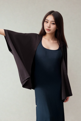 A woman in a dark sleeveless dress and the Olive Basics Deborah Nursing Kimono Cardigan in Charcoal stands with one arm raised against a plain light background.