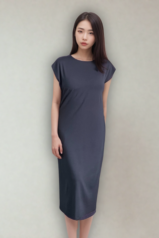 A woman poses in front of a plain light background wearing the Olive Basics Ruth Reversible T-shirt Dress, a short-sleeved, calf-length dark gray dress.