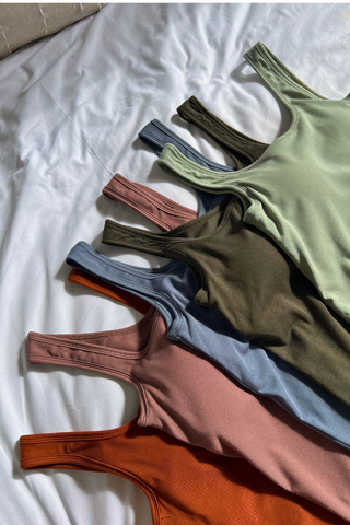 Six Esther Easy Latch Tanks by Olive Basics in green, brown, blue, pink, and orange are neatly arranged on a white bed. Each reversible tank is made from soft bamboo fabric for all-day comfort.