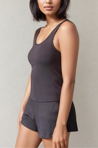 A woman wears the Olive Basics Esther Easy Latch Tank, a sleeveless black reversible neckline top, paired with black shorts against a plain light background.