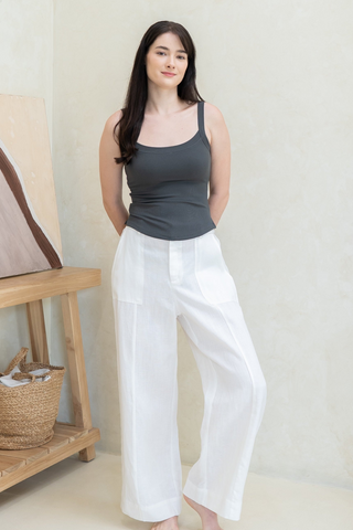 Woman standing indoors wearing a loose-fitting blue shirt and matching culottes with a side slit, set against a bright, minimal room with white walls and curtains.