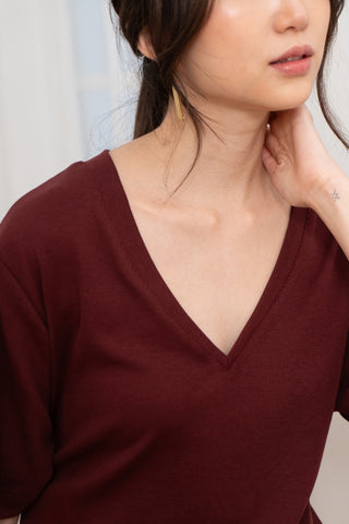 A woman wears the Olive Basics Tabitha Reversible Multi-way Tee in red, featuring a reversible neckline and crafted from soft TENCEL Cotton Rib.