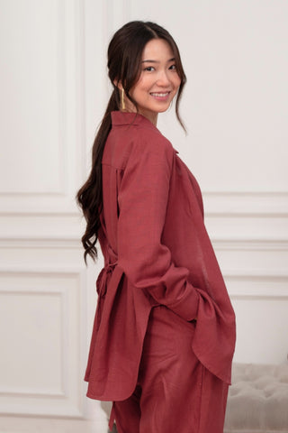 A woman with long dark hair stands sideways and smiles in a bright, white room, wearing the Marie Everyday Shirt in TENCEL™ Linen by Olive Basics with matching pants.