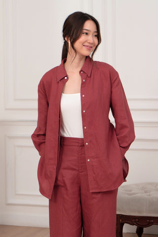 A woman stands indoors with her hands in her pockets, wearing Olive Basics' Marie Everyday Shirt in TENCEL™ Linen and matching pants over a white top. The shirt's structured drape adds elegance against the neutral background.