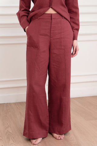 Person wears Olive Basics' Jesse Wide-leg Pocket Pants in TENCEL™ Linen, featuring front pockets and an adjustable waistband, standing barefoot on a wooden floor against a white paneled wall.