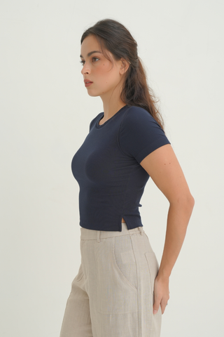 Profile view of a woman wearing a navy Olive Basics Diana Padded Tee and tan trousers.