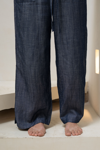 A person stands barefoot indoors wearing Olive Basics’ Bella Multi-Pocket Drawstring Pants, made with a dark blue TENCEL linen blend and featuring a relaxed fit.