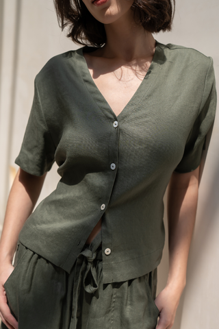 A woman wearing the Olive Basics Bella Multi-way V-neck Shirt in dark green stands against a light background, paired with matching drawstring pants.