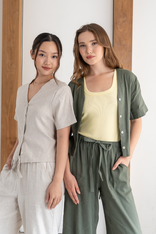 Two women stand side by side indoors, wearing casual, loose-fitting outfits in neutral and green tones. One wears the Bella Multi-way V-neck Shirt from Olive Basics, featuring a nursing-friendly design, as they look at the camera.
