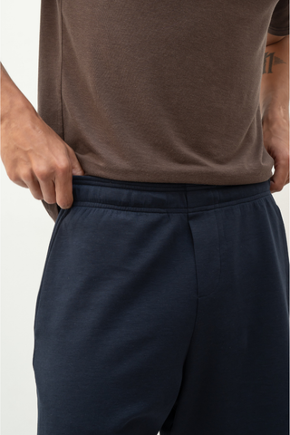 A person wearing Olive Basics Noah Multi-Pocket Stretch Shorts and a brown shirt places their right thumb inside the waistband of the shorts.