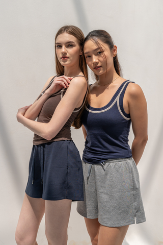 Two women stand side by side against a plain light background, wearing Olive Basics’ Chloe Braless Reversible Tanks and casual shorts. Crafted from soft TENCEL™ Wool Spandex, the tanks provide comfort and versatility as the women face the camera with relaxed expressions.