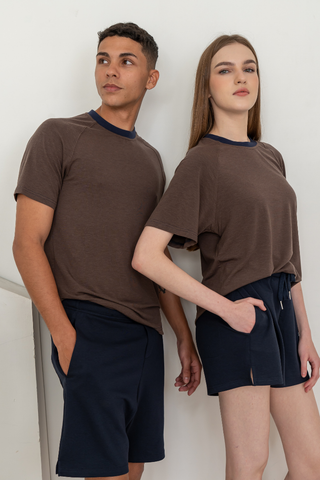 Two people stand indoors against a white wall, wearing brown shirts paired with the Olive Basics Charissa Gentle Waist Pocket Shorts in navy.