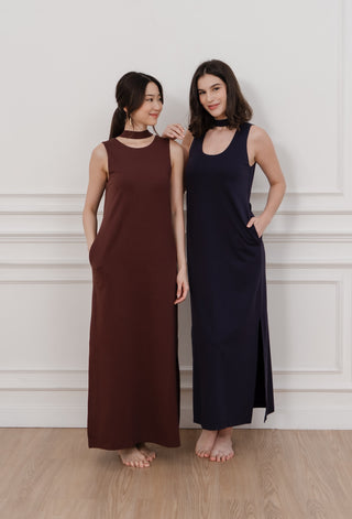 Two women wearing long dresses standing against a white wall.