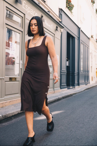 Woman in a brown dress walking on a street with a building in the background