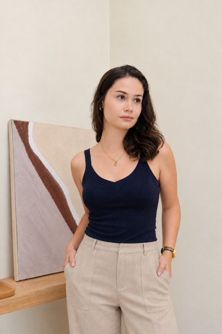 A woman wearing a navy Diana V-neck Reversible Padded Tank and tan trousers with her hands in her pockets.