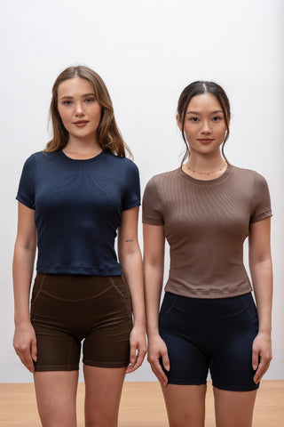 Two women stand side by side against a plain light background, each wearing the Olive Basics Diana Padded Tee in navy paired with high-waisted shorts.