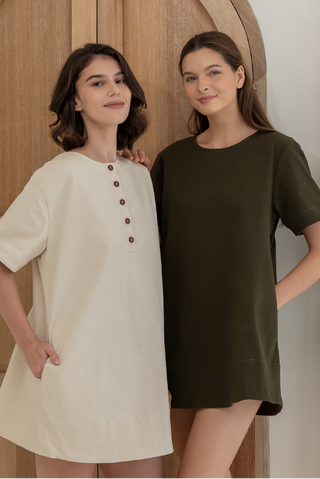 Two women standing side by side in front of a wooden door, wearing short-sleeve dresses.