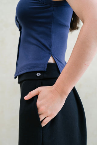 A person models the Olive Basics Grace Reversible Button Tank in navy with black pants, standing sideways with one hand in their pocket.