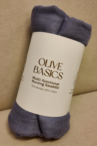 A rolled-up Olive Basics Multi-functional Nursing Swaddle in Ash Blue is displayed on a beige surface, ideal as a nursing cover or breathable baby blanket.