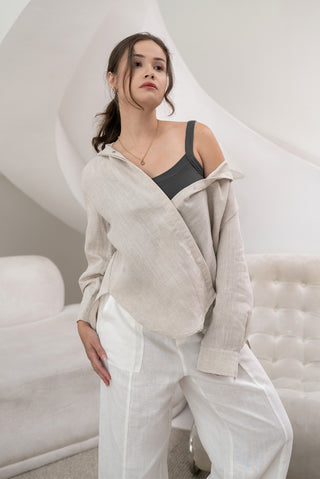 A woman stands in a modern, neutral-toned room wearing the Olive Basics Marie Everyday Shirt in TENCEL™ Linen over a black top and white pants, showcasing the shirt’s structured drape and versatile style.