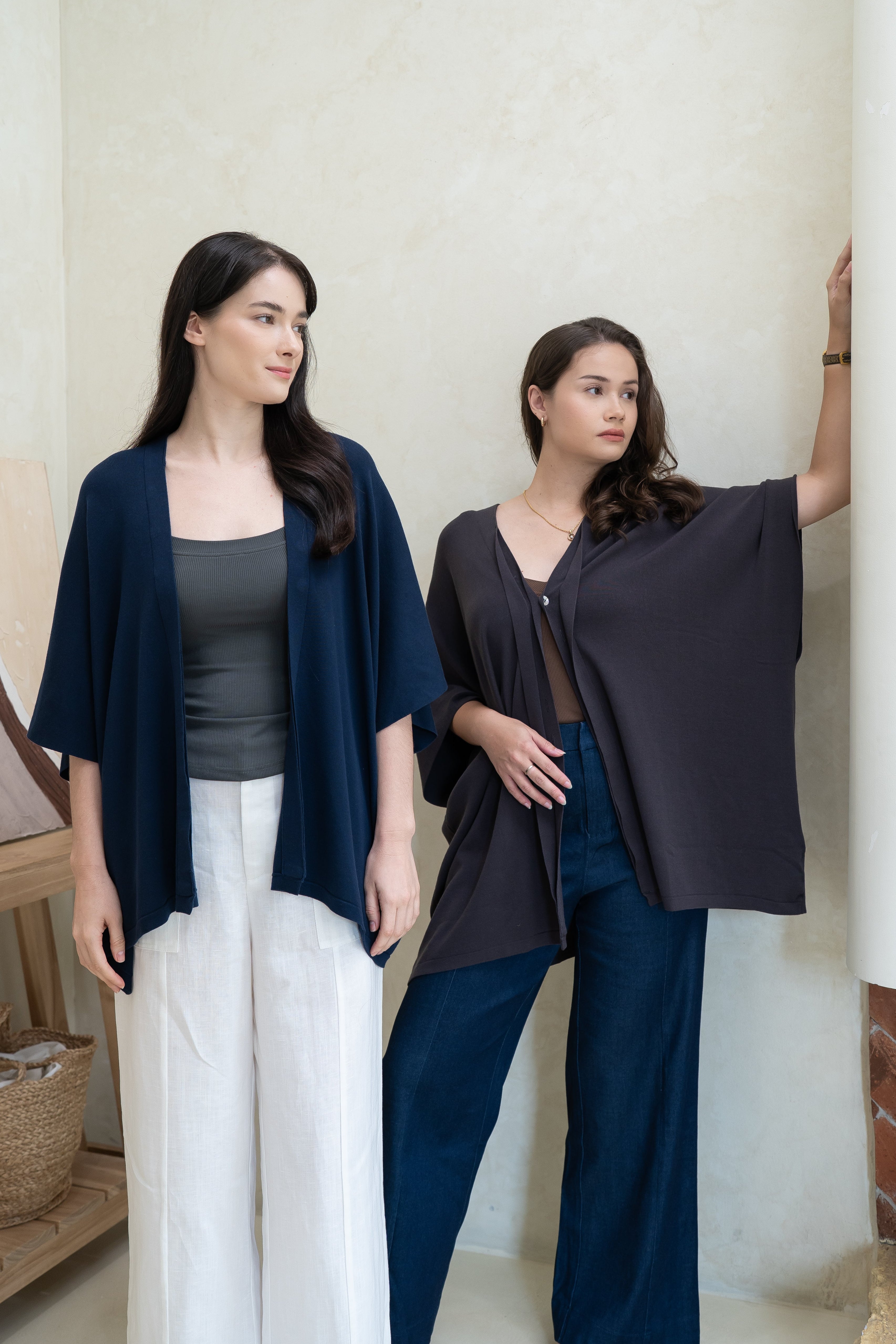 Two women stand indoors against a light wall, both wearing Olive Basics' Deborah Nursing Kimono Cardigans with wide sleeves; one pairs it with white pants, the other with dark blue pants, and both wear dark tops.