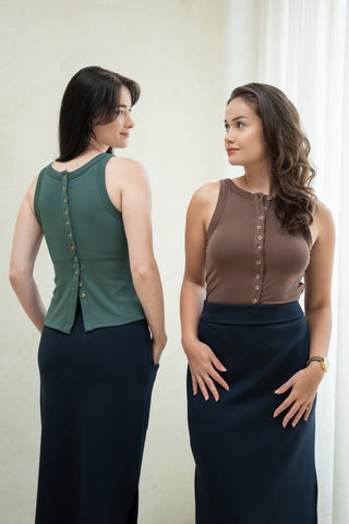 Two women model the Olive Basics Grace Reversible Button Tank indoors, styled with long dark skirts—one faces forward, while the other shows off the tank’s chic back button accents.